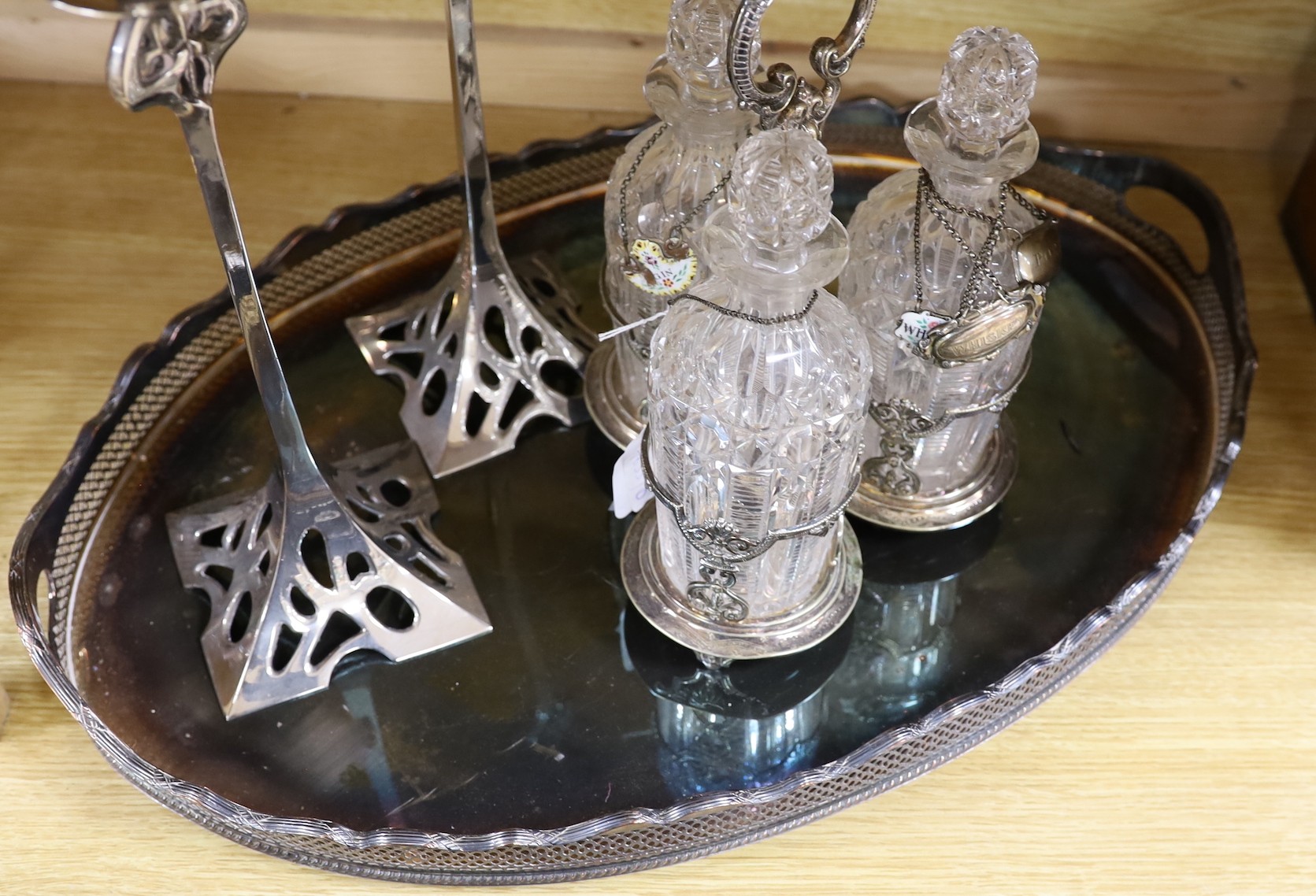 An oval silver plated tray, a three bottled tantalus and a pair of candlesticks, a silver ‘Whiskey’ label, two enamelled silver labels ‘Gin’ and ‘Whisky’ and two plated labels